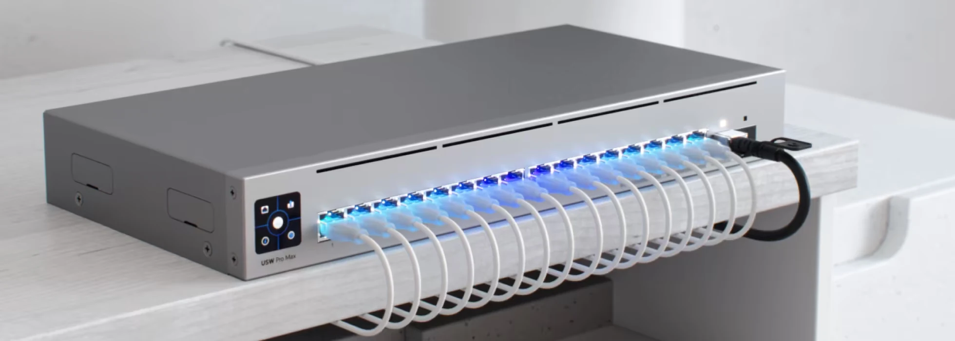 Szary przełącznik sieciowy z podłączonymi przewodami Ethernet i świecącymi na niebiesko diodami.