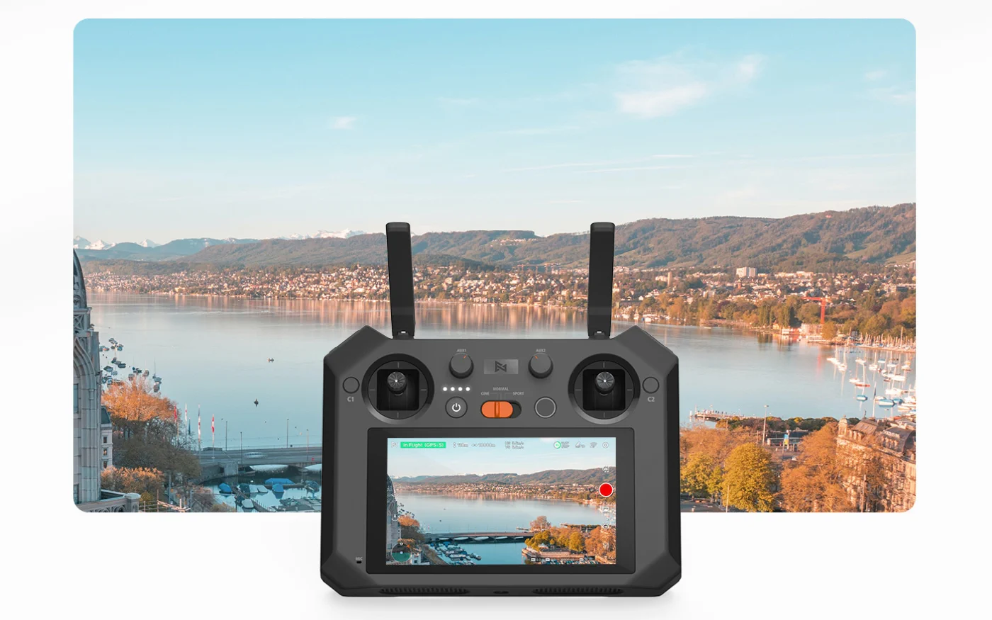 Controlador para dron fimi con pantalla integrada, vista de ciudad con lago y montañas al fondo, el controlador está en primer plano.
