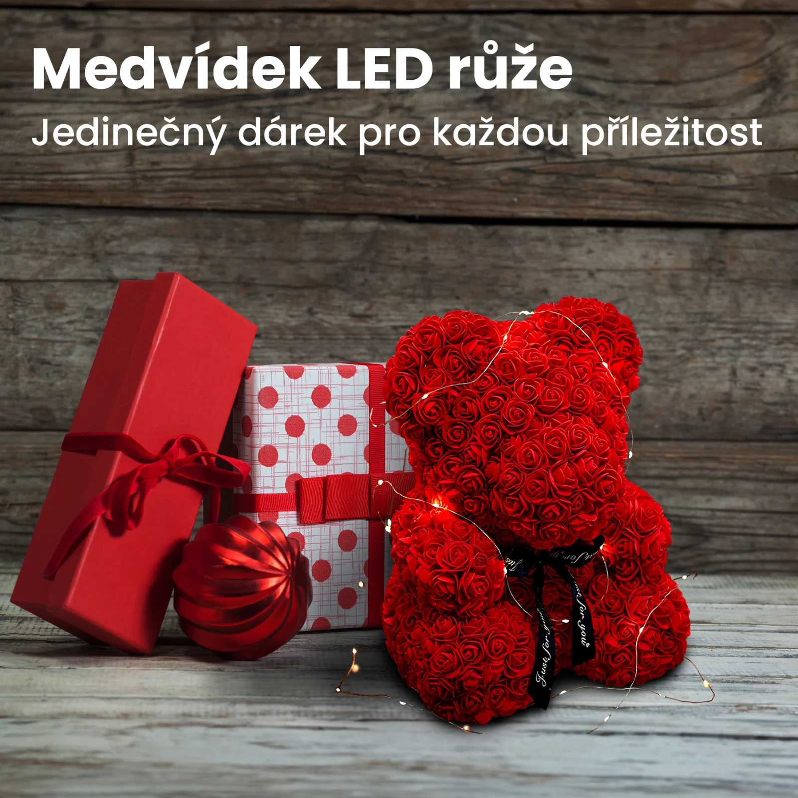 Medv&iacute;dek s červenou růž&iacute;, zabalen&yacute; do LED světel, stoj&iacute; vedle dvou d&aacute;rkov&yacute;ch krabiček a cetky.