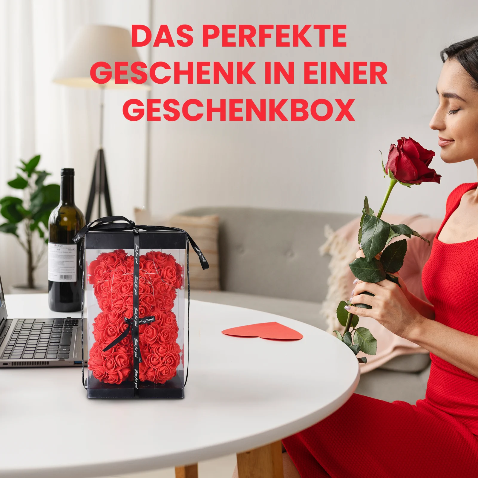 Eine Frau in einem roten Kleid schnuppert an einer roten Rose und sitzt an einem Tisch mit einem Teddybär aus Rosen, der in einer durchsichtigen Schachtel verpackt ist.