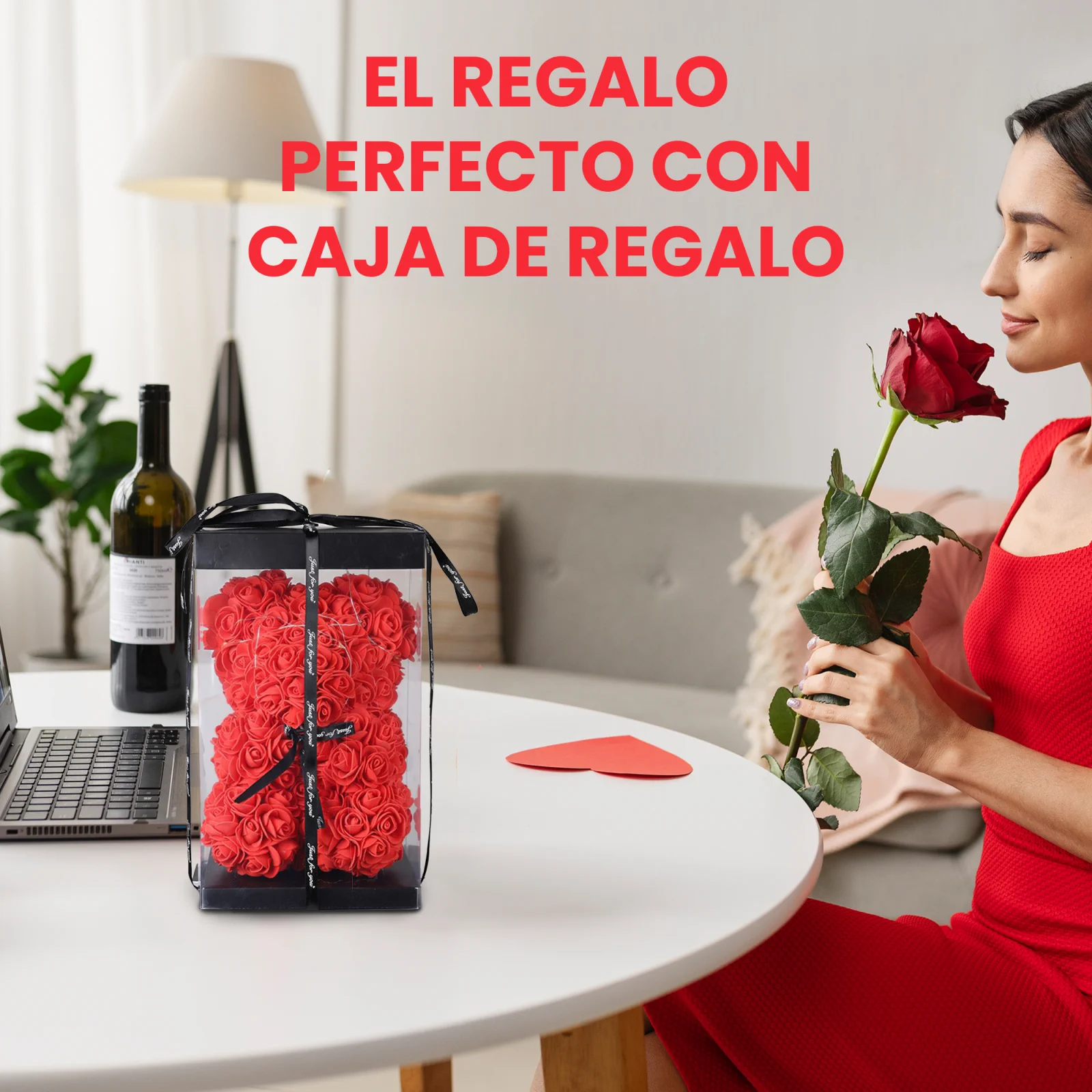 Una mujer con un vestido rojo huele una rosa roja, sentada a una mesa con un osito de peluche hecho de rosas, envuelto en una caja transparente