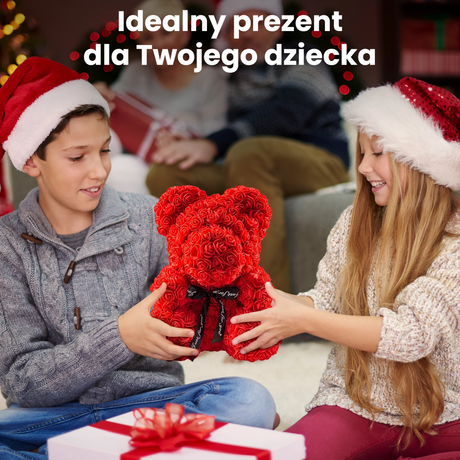 Dos niños sonrientes con gorros de Papá Noel, un niño y una niña, sostienen juntos un osito de peluche rojo con rosa.