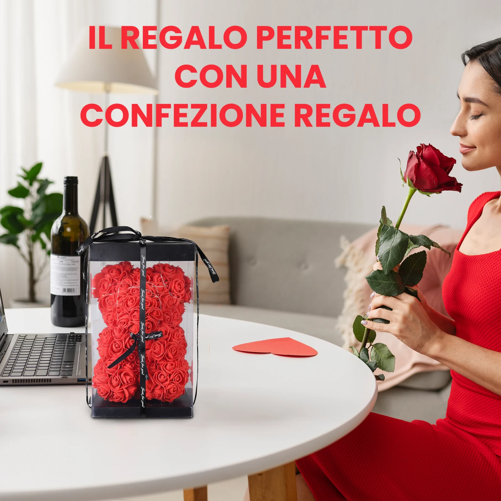 Una donna in abito rosso annusa una rosa rossa, seduta a un tavolo con un orsacchiotto fatto di rose, avvolto in una scatola trasparente