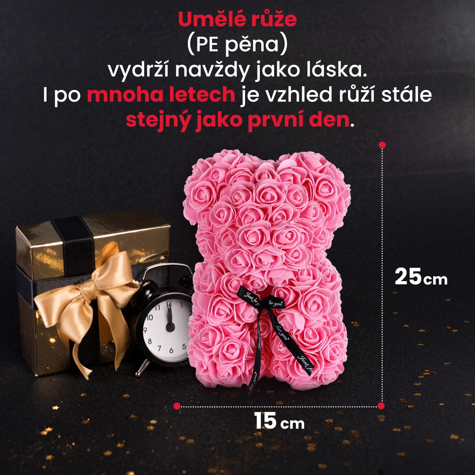 růžový růžový medvídek stojí vedle zlaté dárkové krabičky a černých hodin.