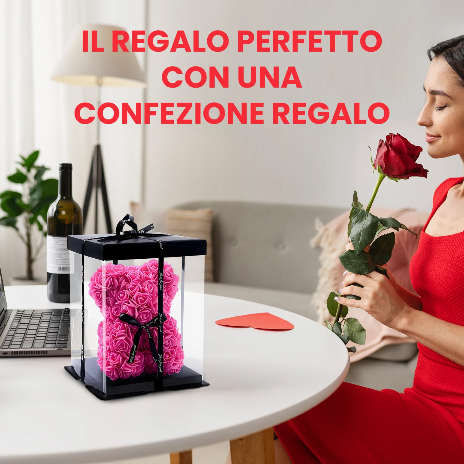 Una donna vestita annusa una rosa rossa mentre è seduta a un tavolo con un orsacchiotto fatto di rose, avvolto in una scatola trasparente