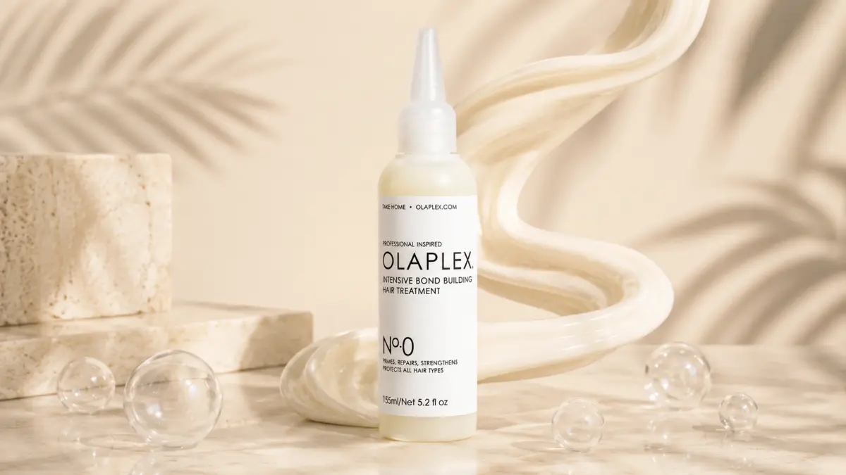 Bottle of hair treatment on a light background with a wavy strand of hair and glass spheres