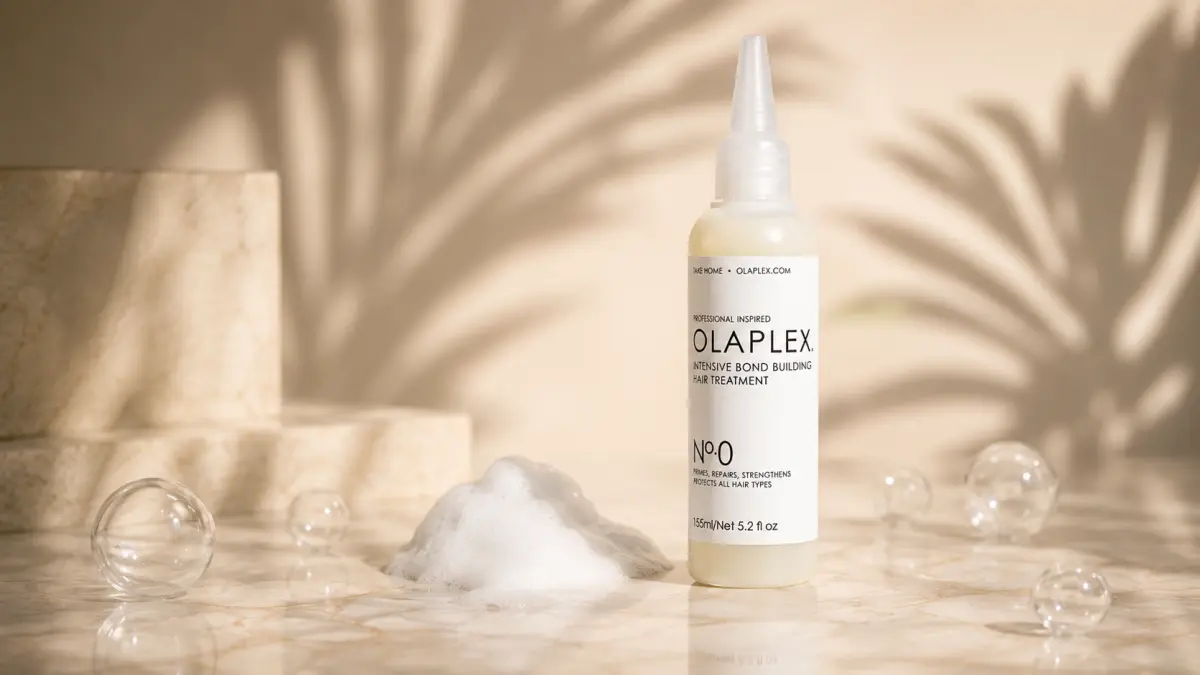 Bottle of hair product placed on a marble countertop next to foam and decorative spheres