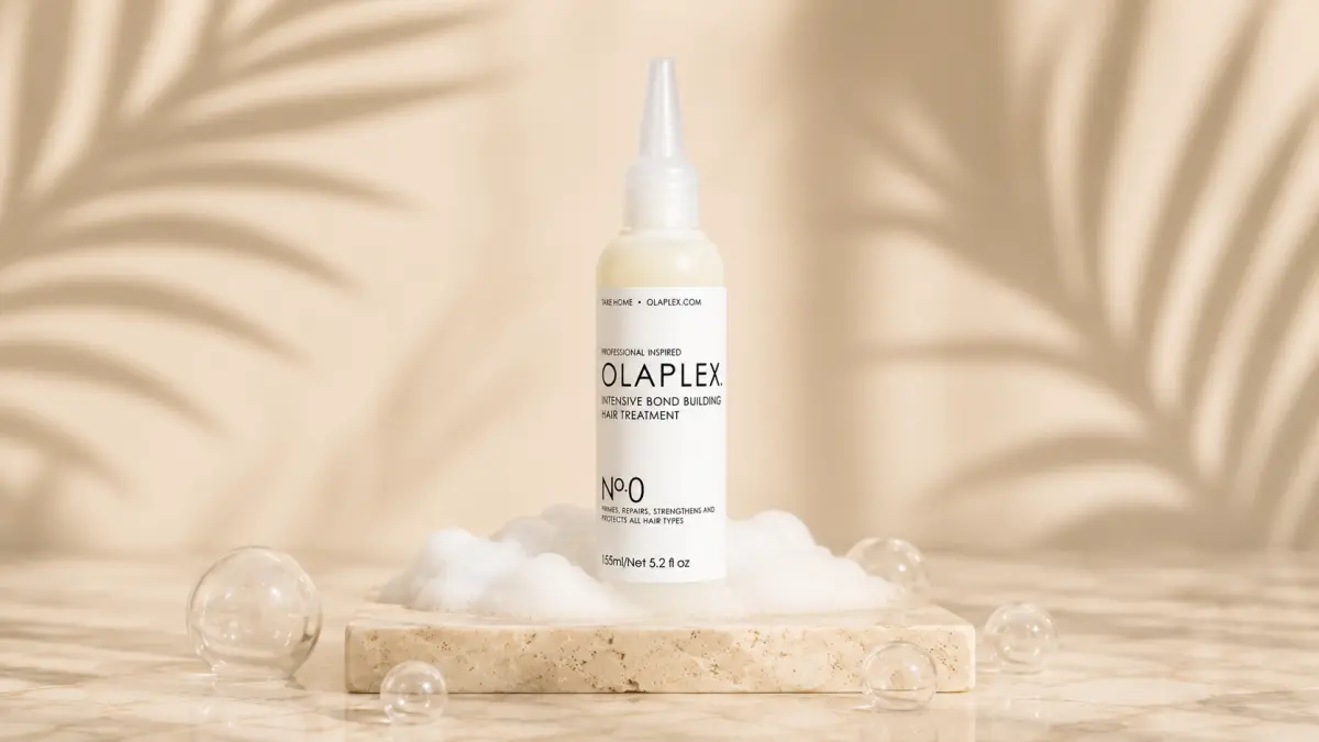 Bottle of hair treatment standing on a stone base surrounded by foam and light shadows