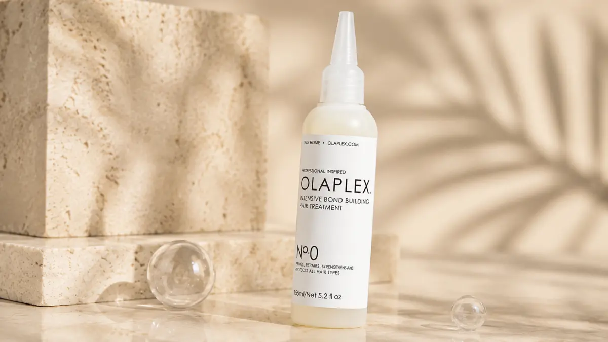 Bottle of hair product on a light countertop next to stone blocks and glass spheres