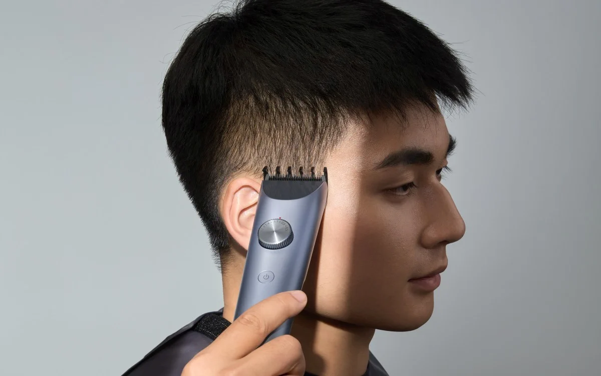 Mężczyzna używa niebiesko-szarej maszynki do strzyżenia xiaomi hair clipper 2, aby przyciąć włosy nad uchem.