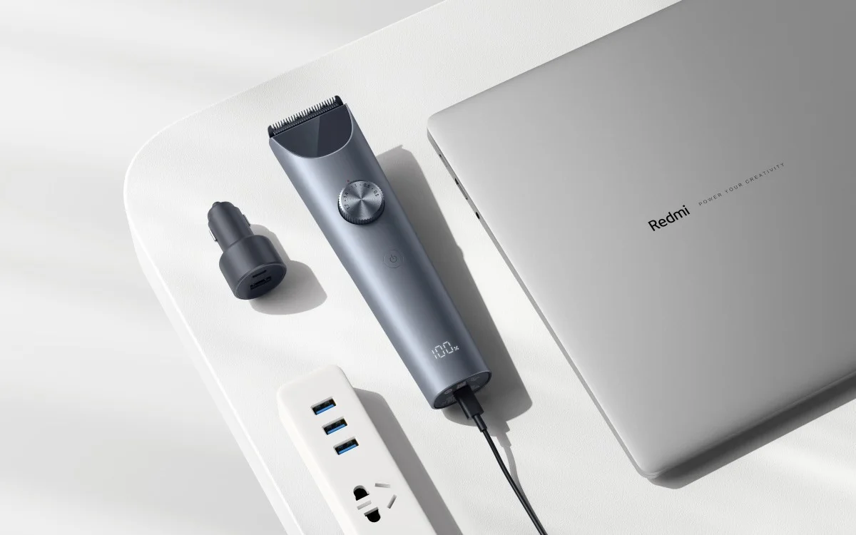 Maszynka do strzyżenia xiaomi hair clipper 2 ładuje się na białym biurku, obok laptopa Redmi, ładowarki samochodowej i listwy zasilającej