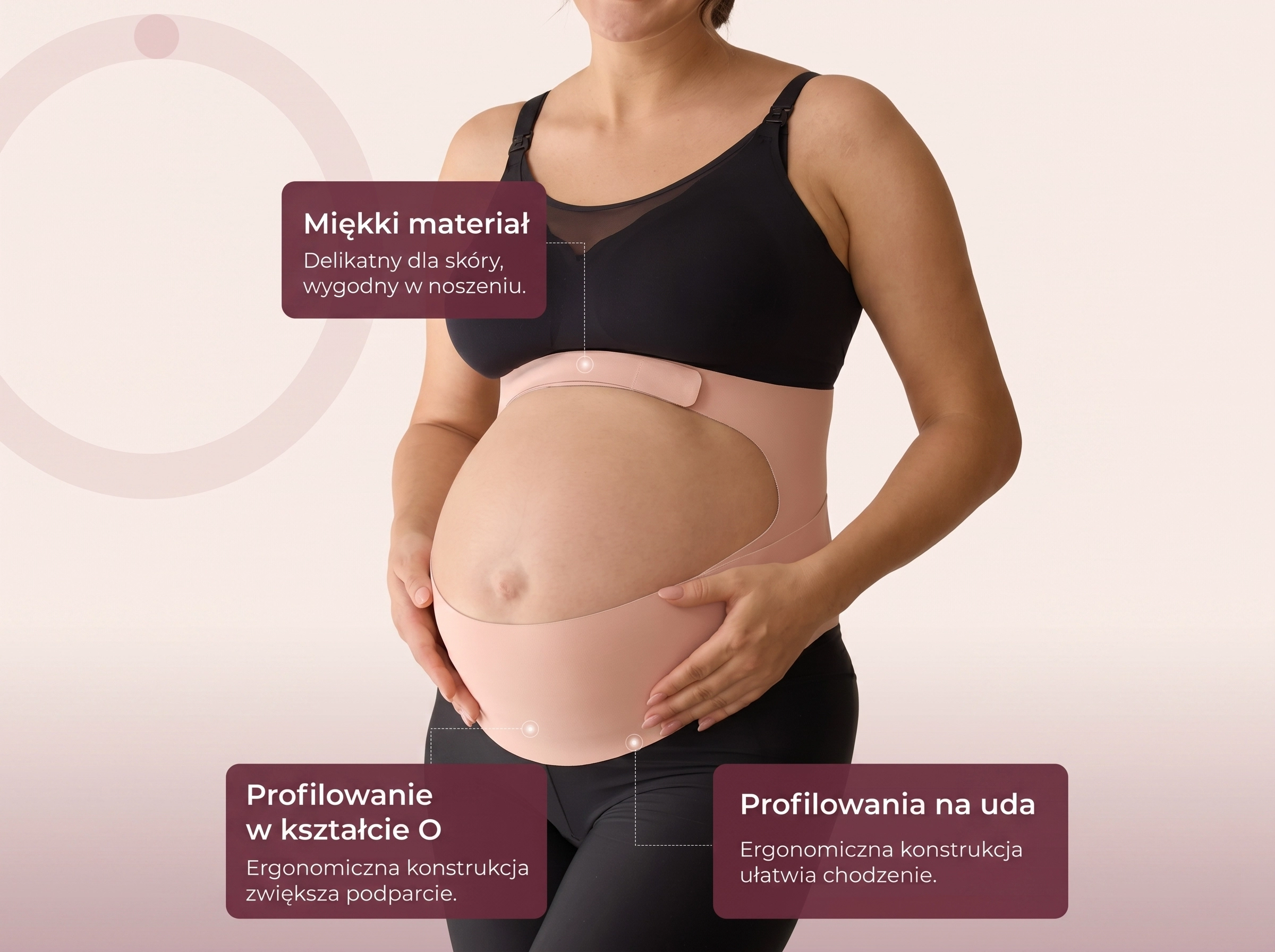 Mulher grávida com top preto e cinto de gravidez bege, de pé ereta, com as mãos na barriga, em frente a uma parede clara.
