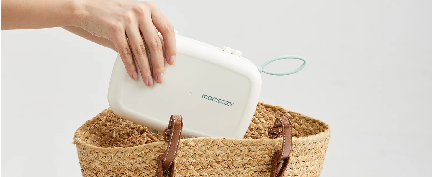 Uma mão a colocar um estojo branco com o logótipo Momcozy num cesto de viagem entrançado.