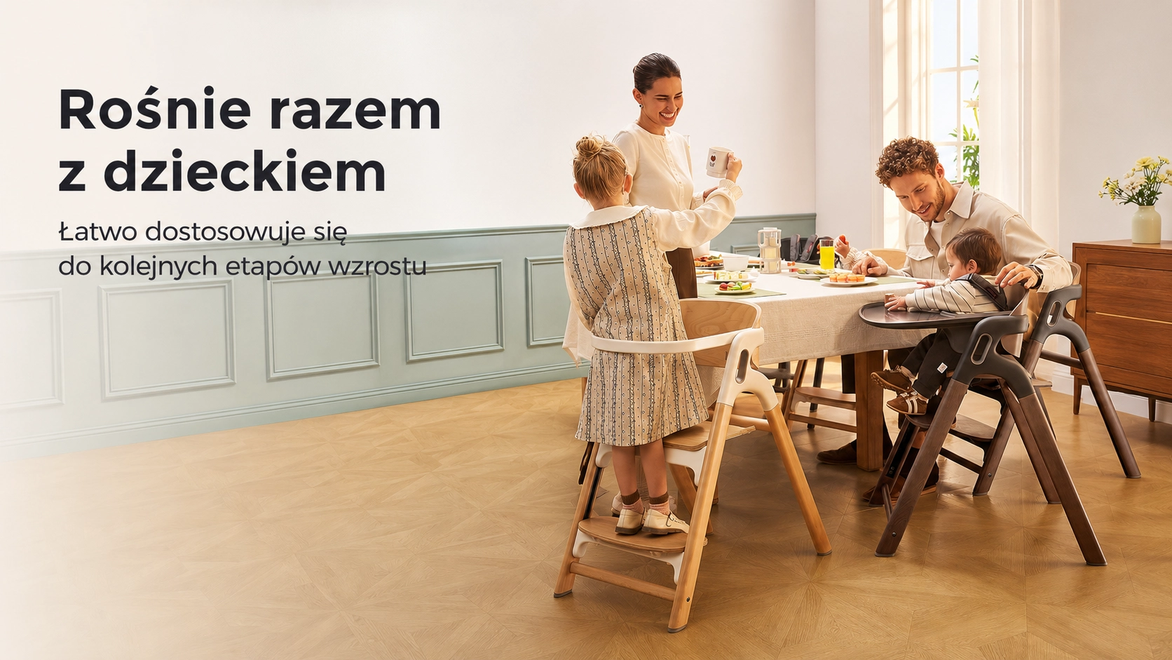 Rodzina przy stole, gdzie małe dziecko siedzi w ciemnym krzesełku, a starsza dziewczynka stoi na wersji z podestem.