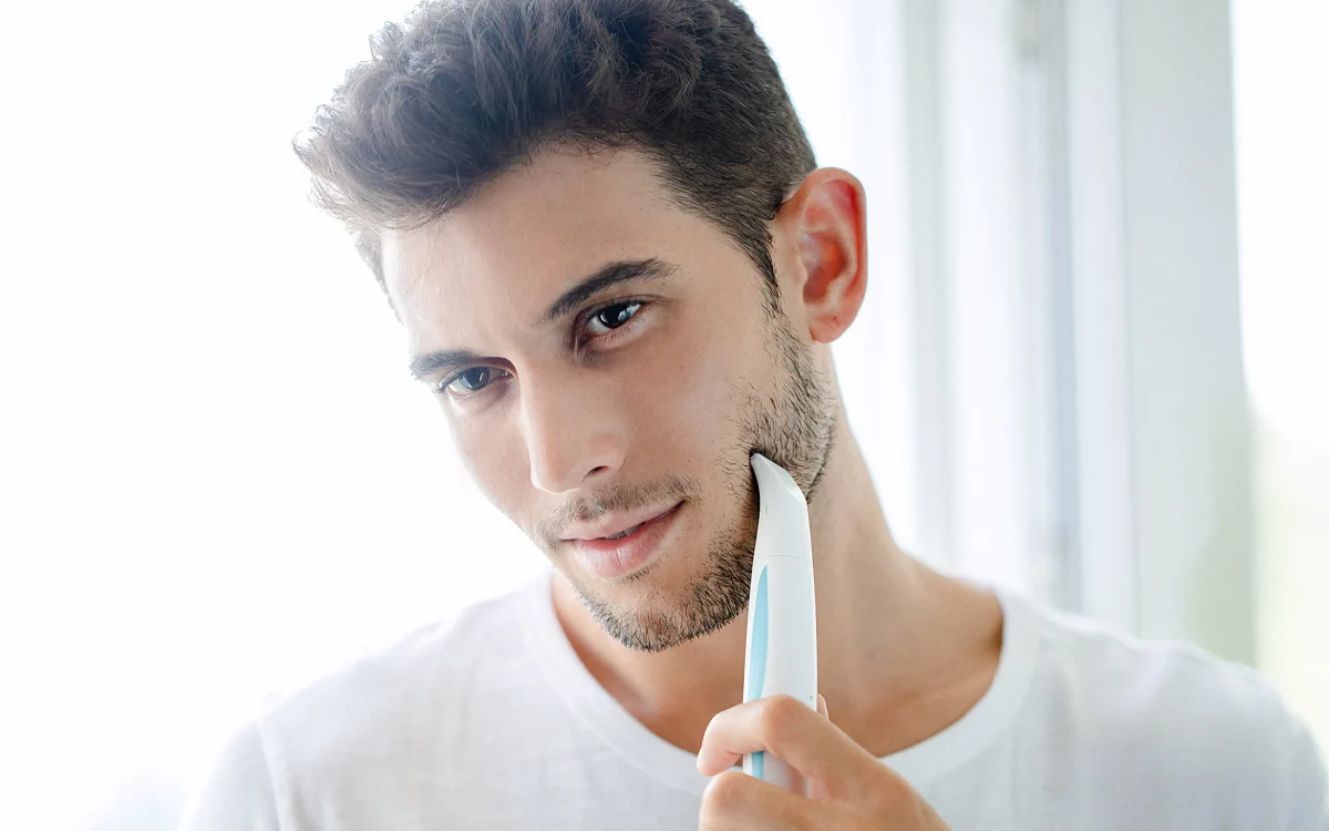 un hombre moreno con vello facial utiliza el Mini Personal Groomer de dix frente al espejo