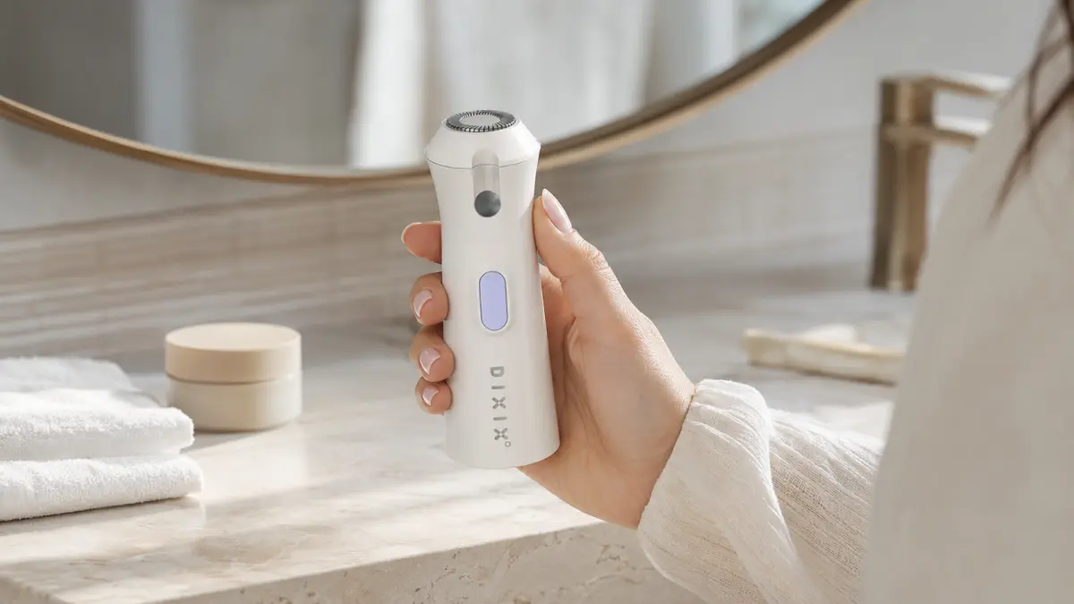 Bílý DIXIX Mini Hair Remover držený v ruce před zrcadlem