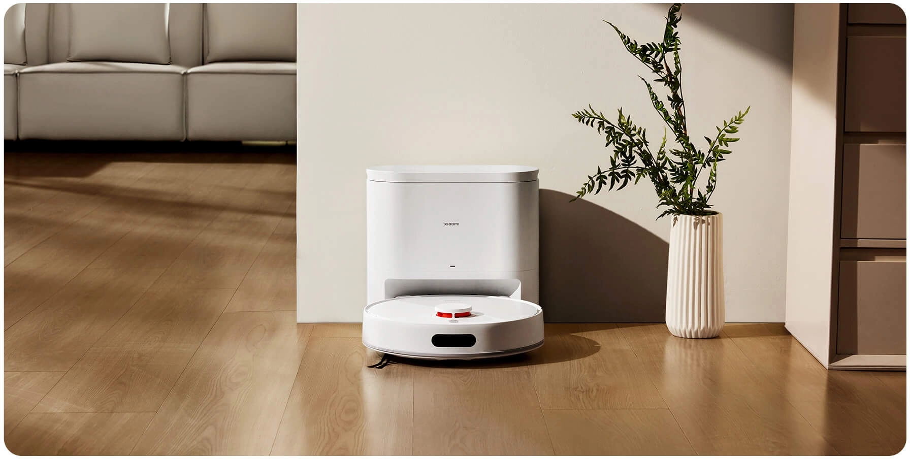 Xiaomi Robot Vacuum H40 находится рядом с зарядной станцией на фоне простого, элегантного интерьера с растением в вазе