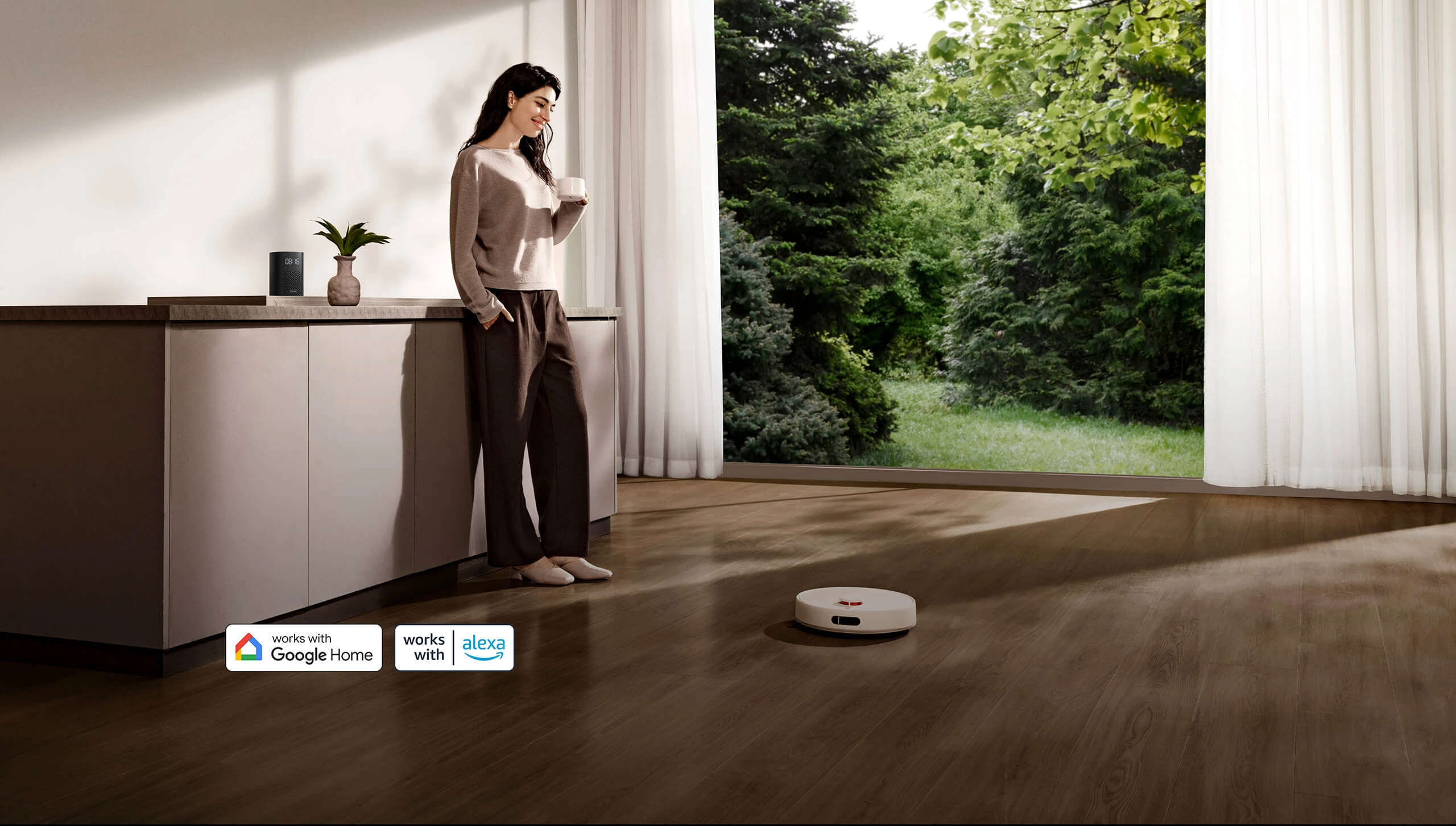 Женщина стоит у кухонной столешницы с чашкой в руках, пока Xiaomi Robot Vacuum H40 пылесосит рядом.