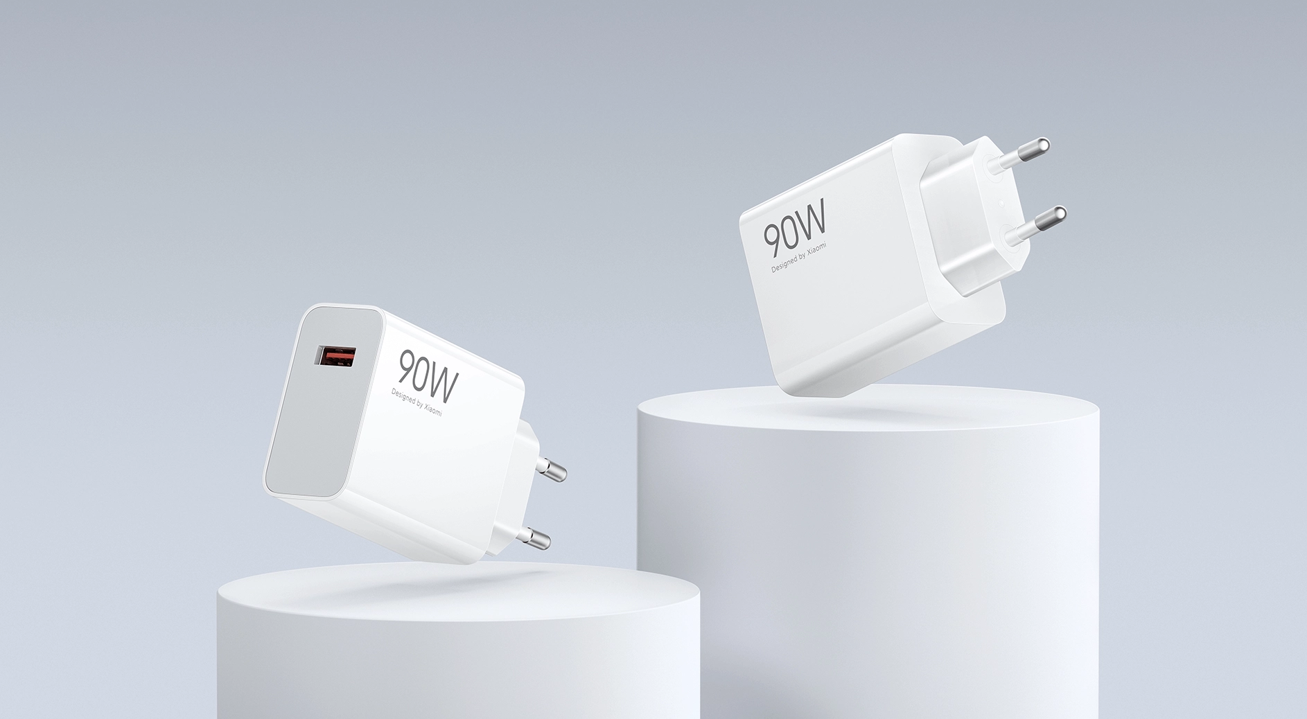Dwie białe ładowarki sieciowe Xiaomi 90W HyperCharge Combo EU z wtyczką europejską i portem USB-C, ustawione na cylindrycznych postumentach na jasnym tle