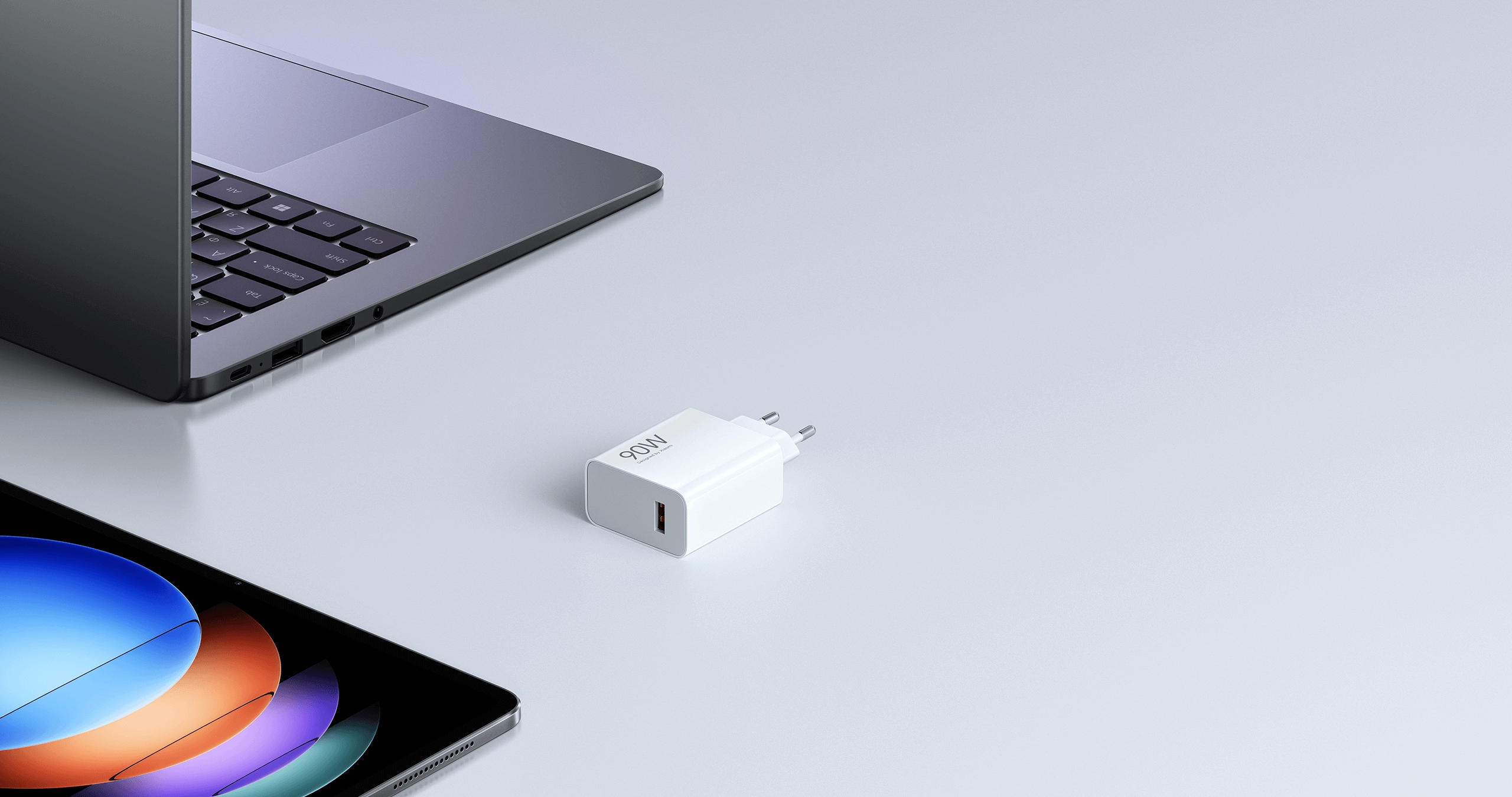 Ładowarka Xiaomi 90W HyperCharge Combo EU leżąca na biurku obok laptopa i tabletu, przedstawiona w minimalistycznym, srebrno-białym otoczeniu