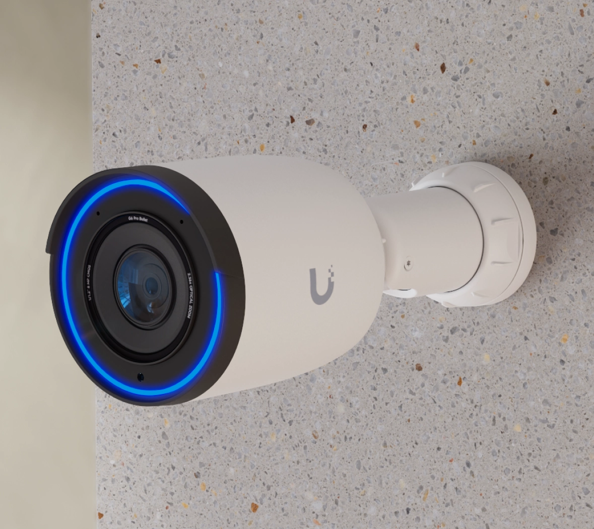 Zainstalowana kamera Ubiquiti UVC-G6 Pro Bullet na ścianie, z niebieskim pierścieniem LED wokół obiektywu