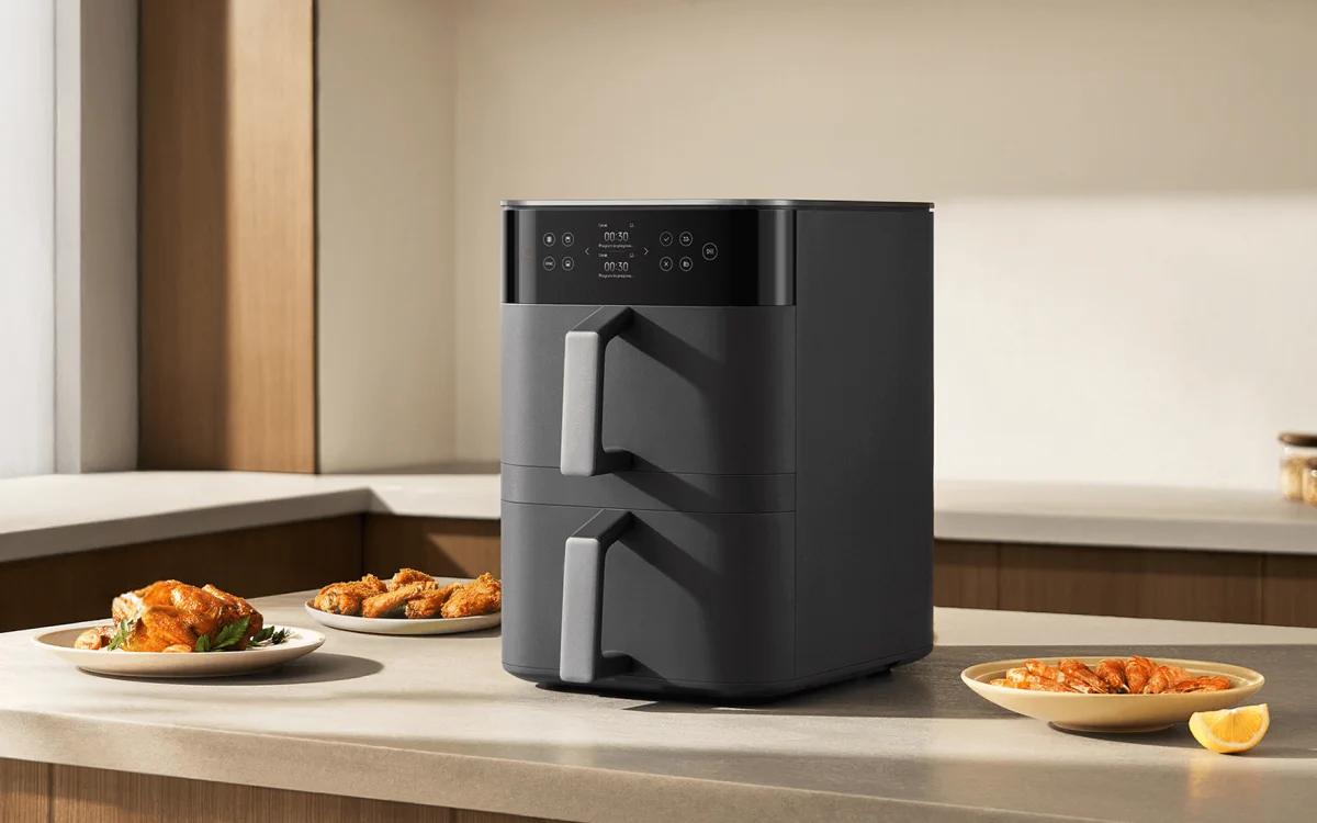 Black Xiaomi air fryer with two drawers standing on a worktop next to plates with roast chicken and prawns