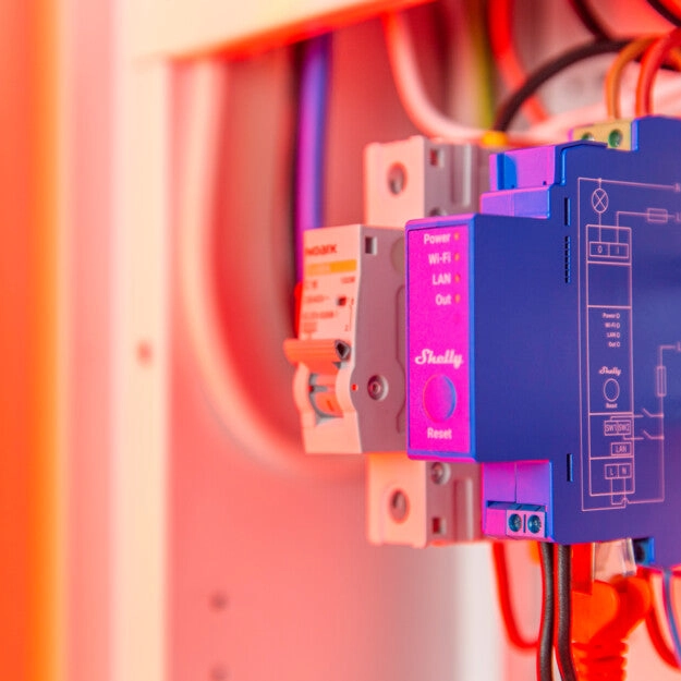 Shelly Pro 1 w szafie rozdzielczej, połączony z kablami, z widocznymi portami LAN i Wi-Fi, gotowy do sterowania urządzeniami elektrycznymi.