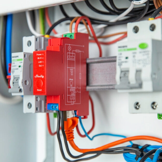 Zbliżenie na urządzenie Shelly zamontowane w panelu elektrycznym, widoczne liczne przewody i złącza