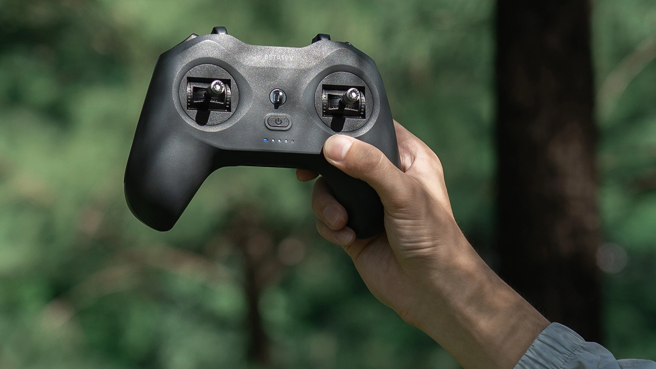 Kontroler BetaFPV w ręku, pokazujący dwa drążki sterujące w plenerze