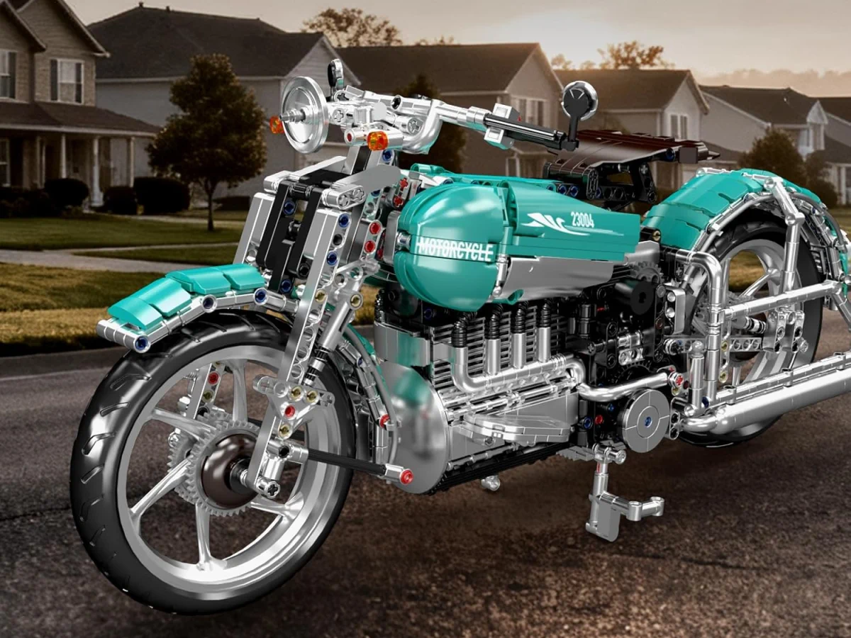 Model of a motorcycle made from building blocks in turquoise and silver, standing on an asphalt road in front of houses