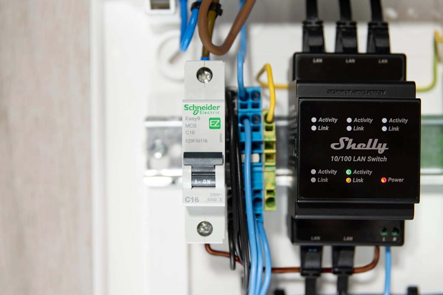 Przełącznik LAN Shelly z aktywnymi diodami LED, podłączony do ściany w obudowie elektrycznej, z widocznymi przewodami