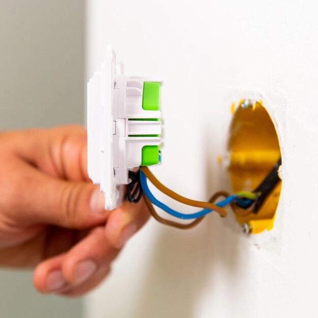 Mężczyzna instaluje włącznik, widoczne przewody elektryczne i pusty montażowy otwór w ścianie
