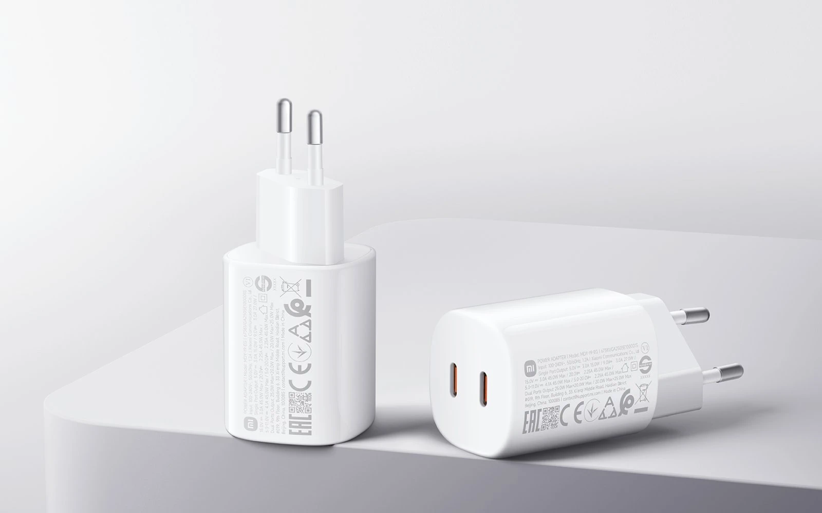 Dois carregadores de rede Xiaomi brancos, um em pé na vertical e outro deitado de frente com duas portas USB-C visíveis