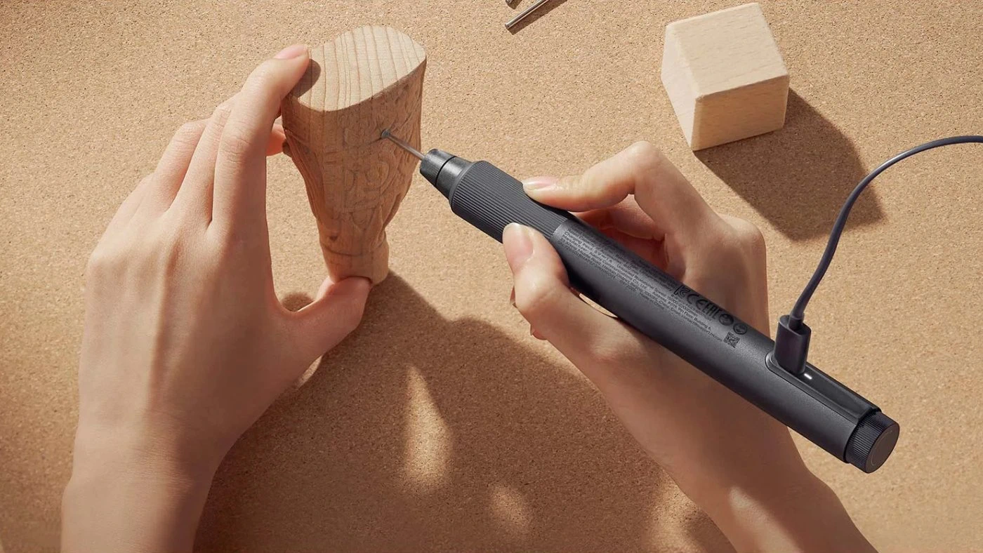 Osoba rzeźbiąca w drewnie za pomocą precyzyjnej szlifierki podłączonej kablem USB-C do ładowania