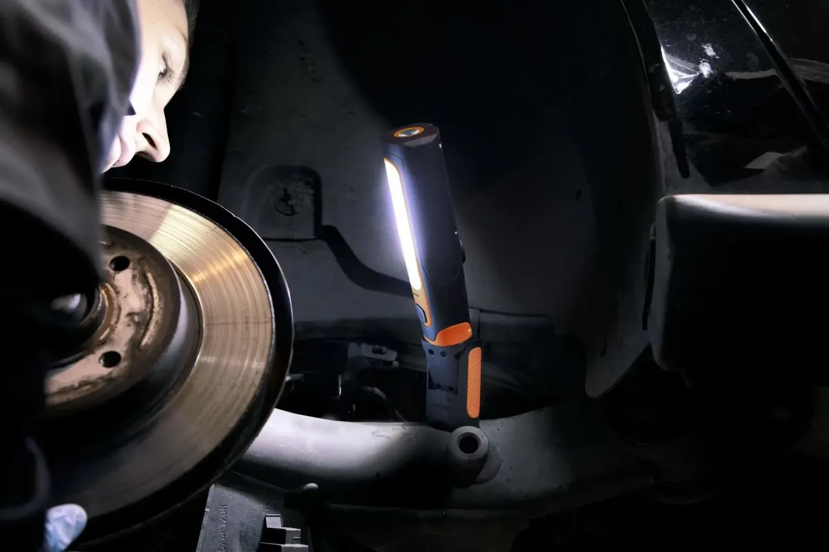 Mechanik oświetlający tarczę hamulcową i elementy zawieszenia samochodu za pomocą pionowej lampy warsztatowej