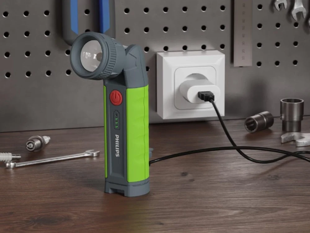 Zielono-szara latarka z łamaną głowicą ładuje się przez kabel USB podłączony do gniazdka na warsztatowym stole
