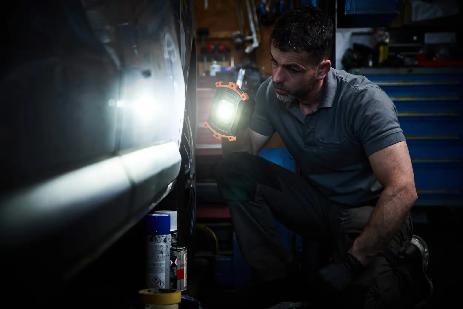 Mechanik w warsztacie oświetla bok samochodu trzymaną w dłoni lampą warsztatową LED