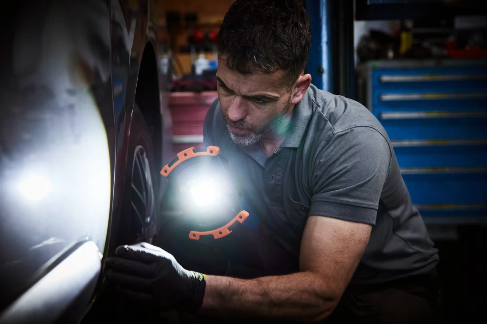 Mechanik w czarnych rękawiczkach oświetla mocnym światłem LED nadkole samochodu podczas inspekcji