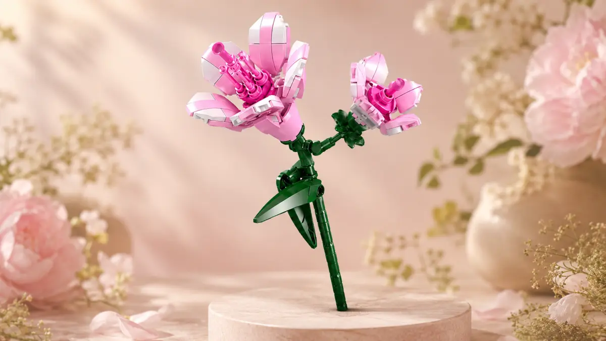 Flor rosa de blocos sobre um pedestal claro, cercada por flores e decora&ccedil;&otilde;es em tons pastel.