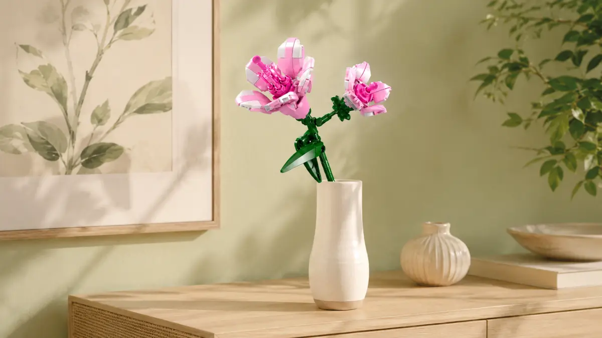 Flor rosa de blocos em um vaso branco, colocada sobre uma c&ocirc;moda de madeira em um interior claro.