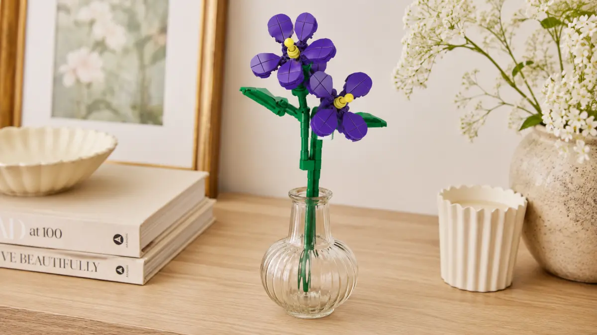 Flor violeta de blocos num vaso transparente sobre uma c&oacute;moda de madeira com decora&ccedil;&otilde;es.