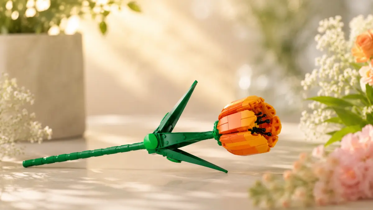 Flor laranja de blocos deitada horizontalmente sobre uma bancada clara entre plantas decorativas.
