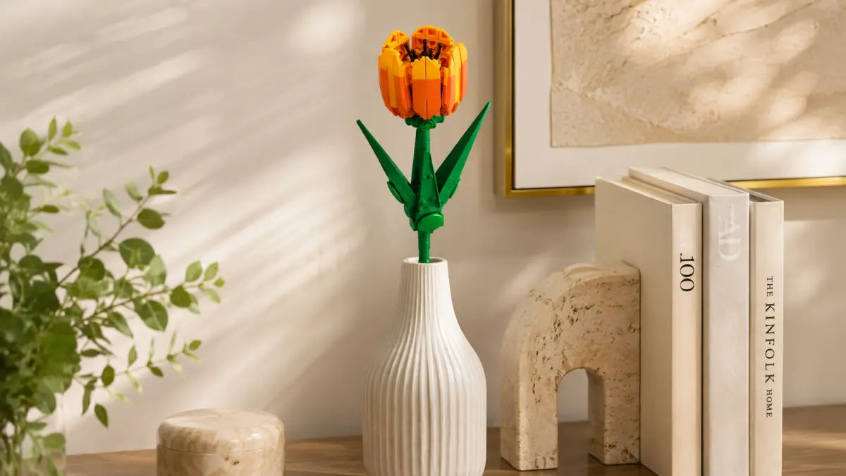 Flor laranja de blocos colocada num vaso branco ao lado de livros e decora&ccedil;&atilde;o.