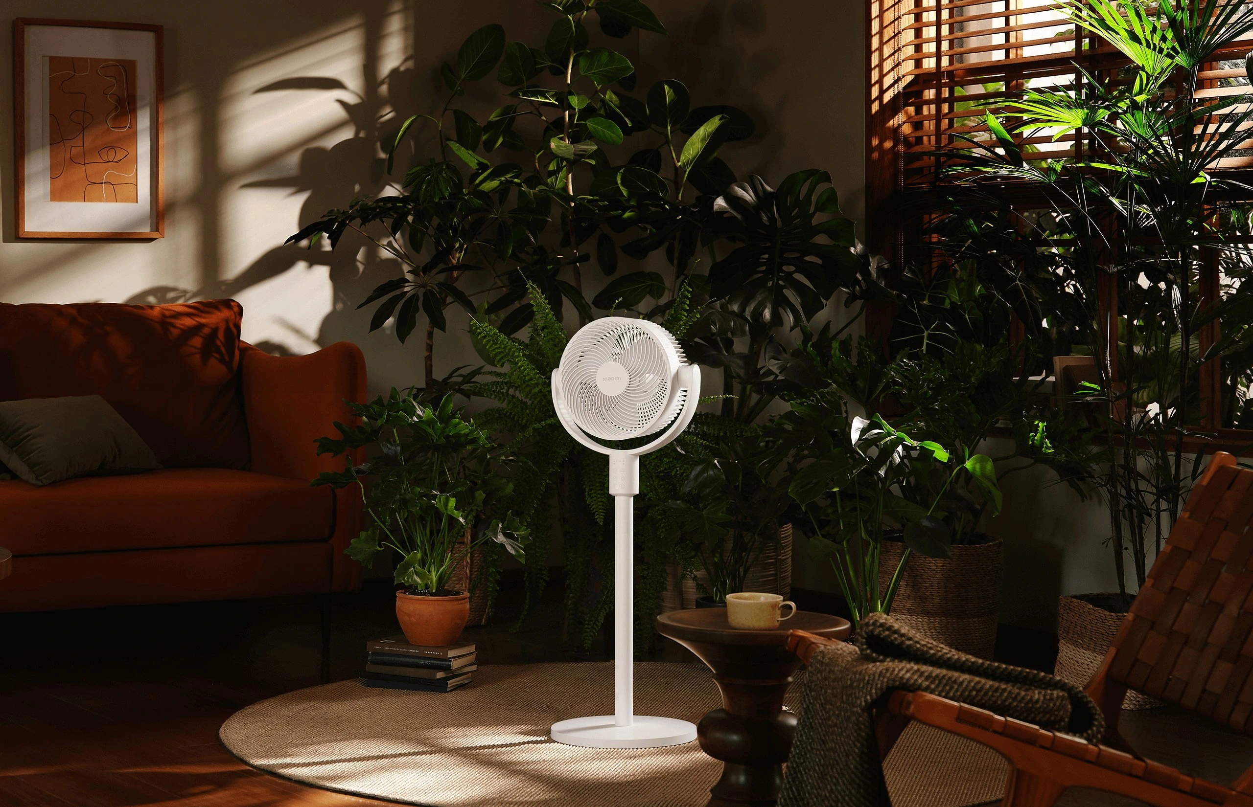 Weißer Standventilator im Wohnzimmer voller grüner Topfpflanzen neben einem braunen Sofa