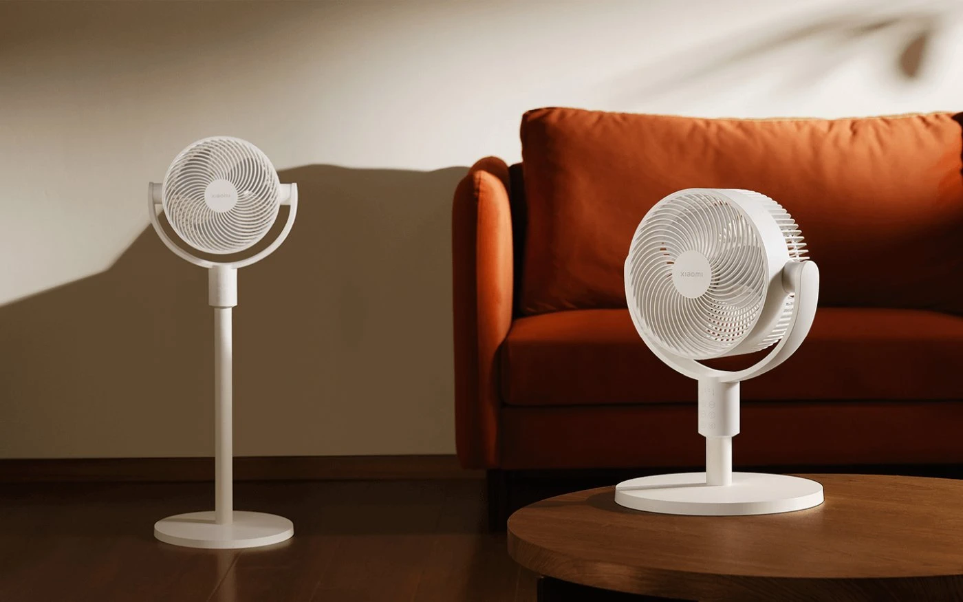 Zwei weiße Ventilatoren neben einem orangefarbenen Sofa zeigen den Höhenunterschied zwischen Stand- und Tischversion
