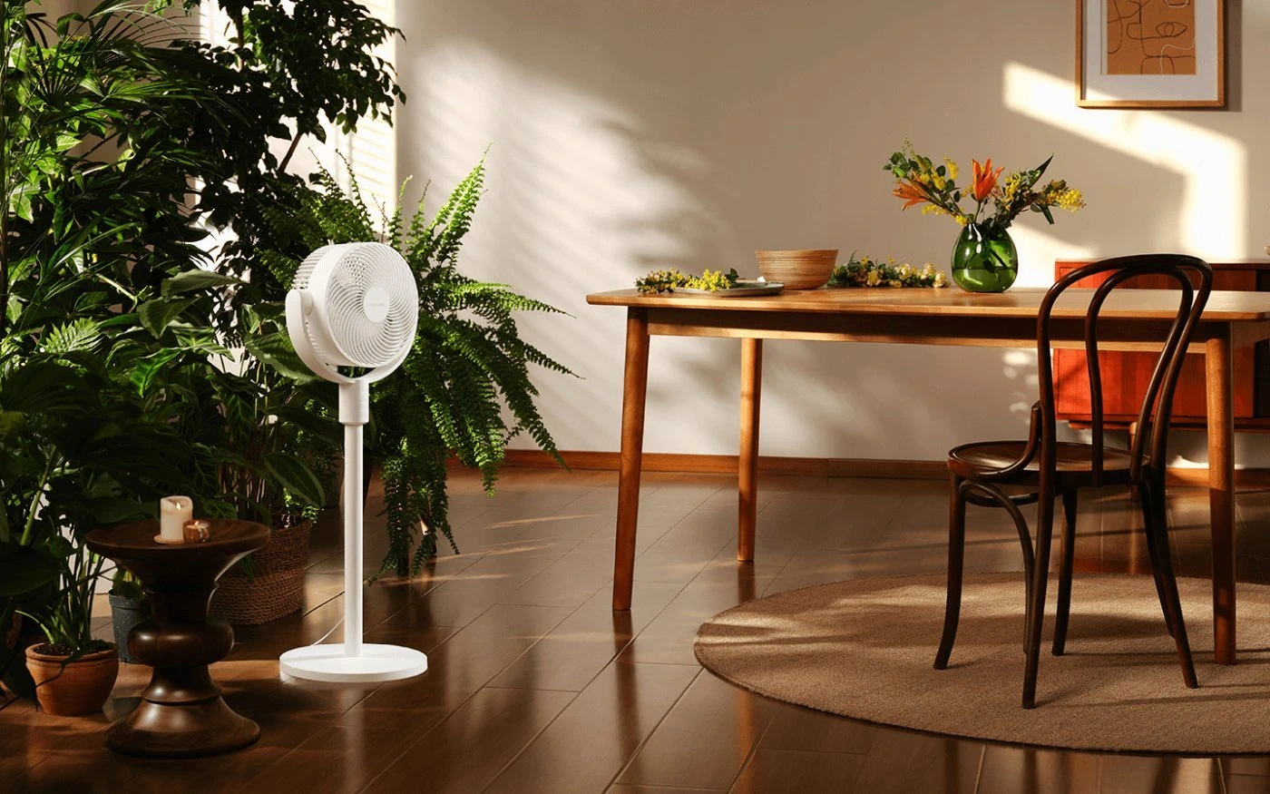 Weißer Standventilator in einem hellen Esszimmer neben einem Holztisch mit Blumen und einem Stuhl