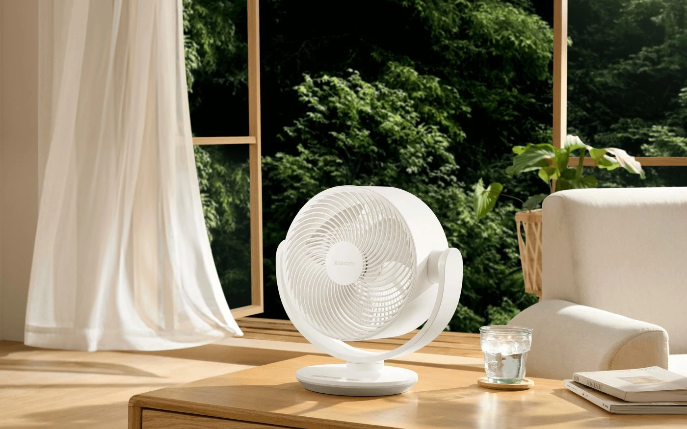 Ventilador Xiaomi blanco sobre una mesa de madera en un salón luminoso con vistas a árboles verdes por la ventana