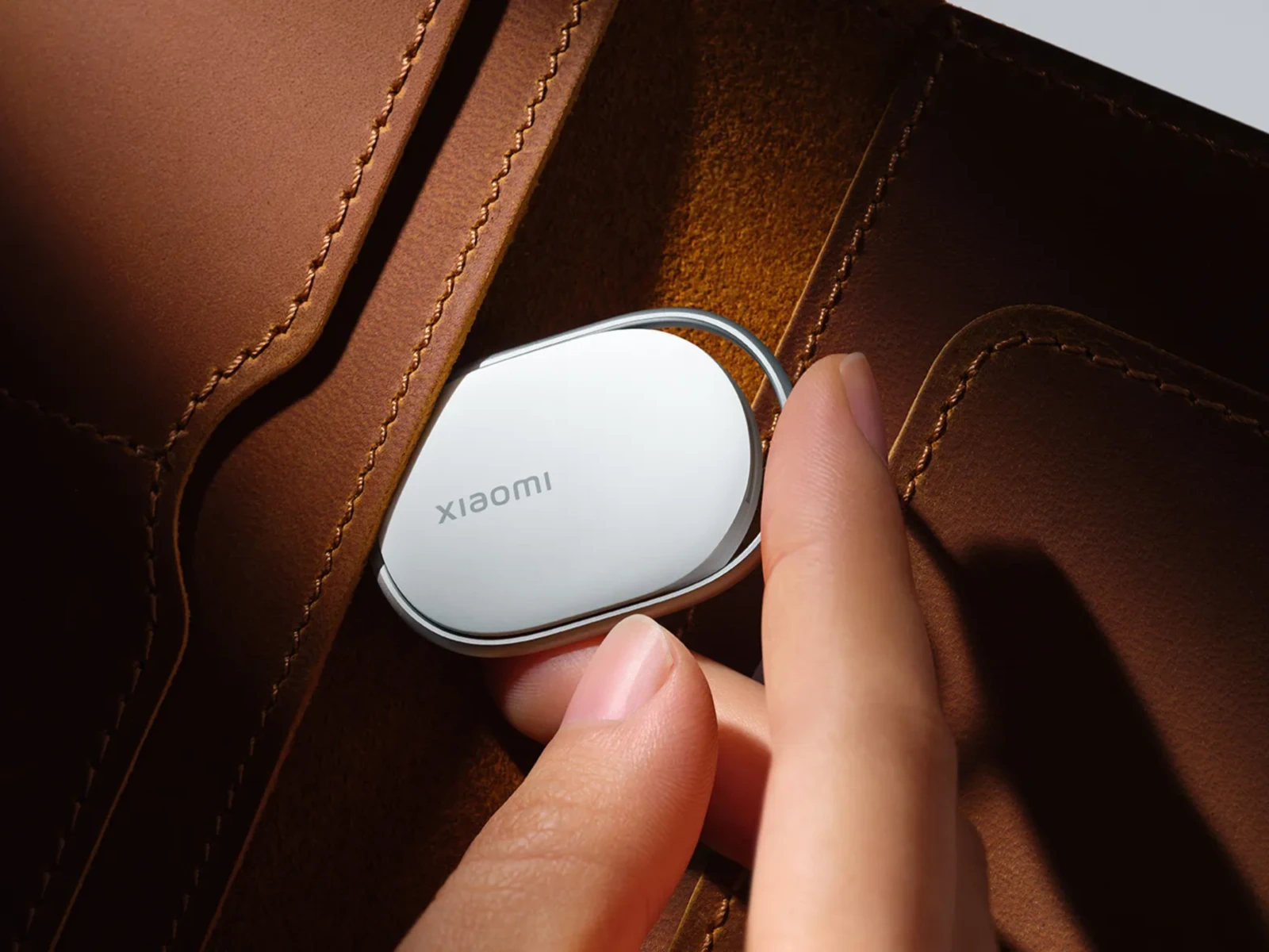 Пальцы вкладывают белый локатор Xiaomi в отделение кожаного коричневого кошелька