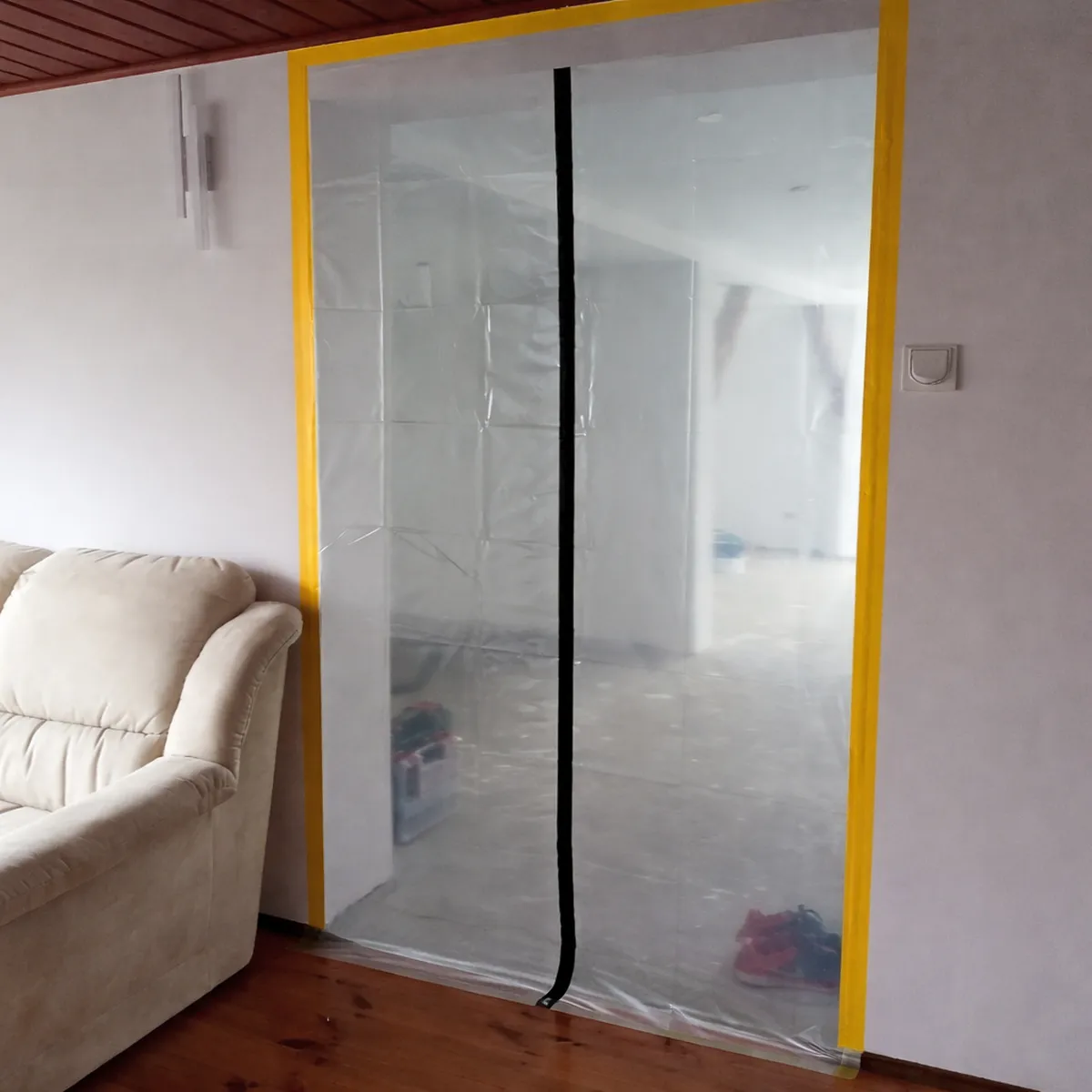 Kurtyna foliowa przyklejona żółtą taśmą do białej ściany oddzielająca salon od remontowanego pokoju