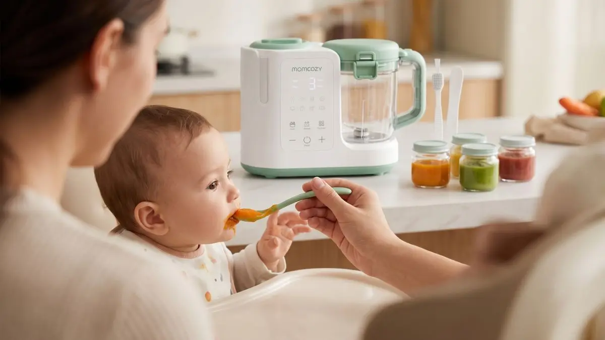 Mãe a alimentar o bebé com uma colher junto ao dispositivo Momcozy para preparar refeições para bebés.